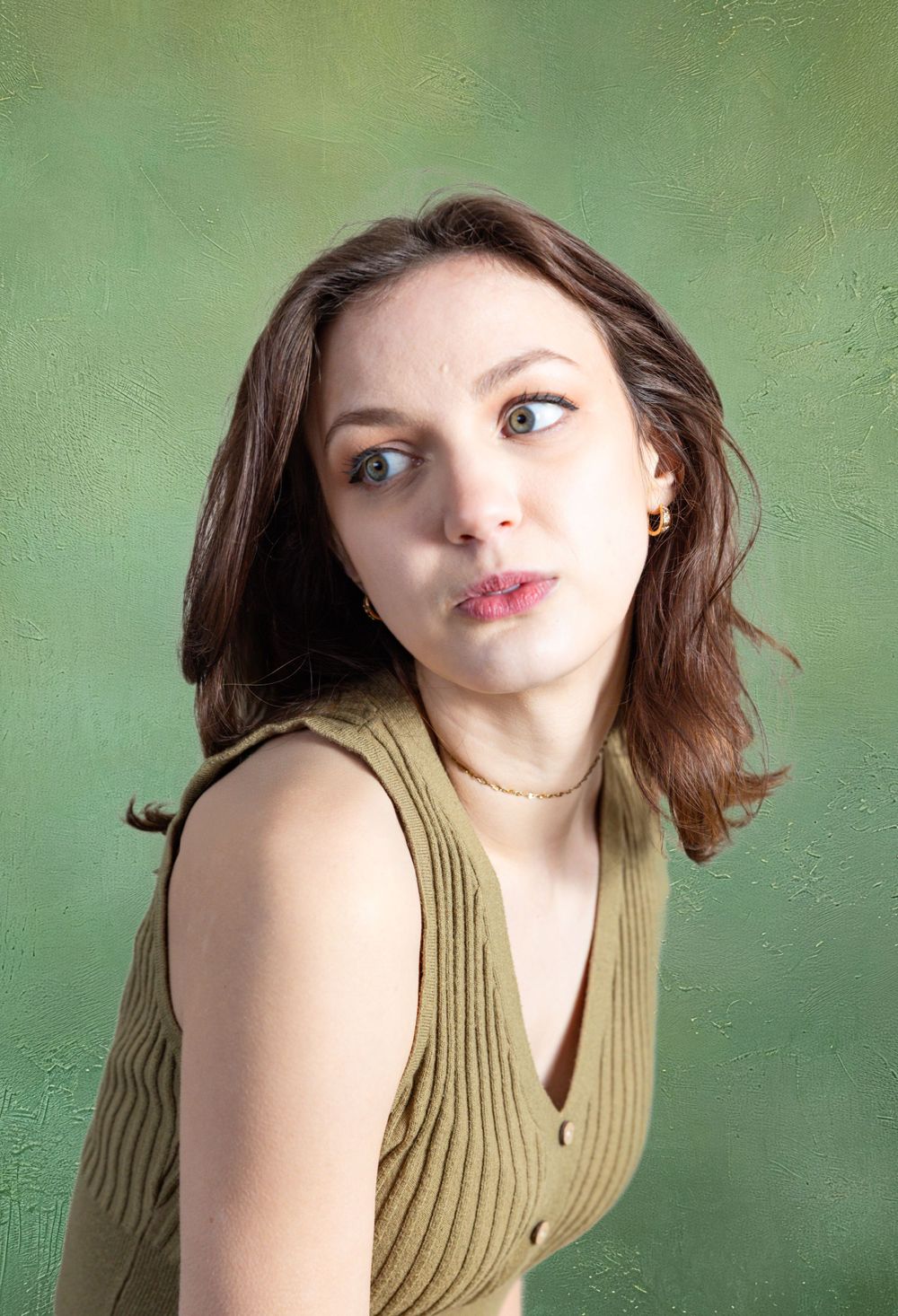 A young brunette woman in a green sleeveless top makes a playful expression on green background.
