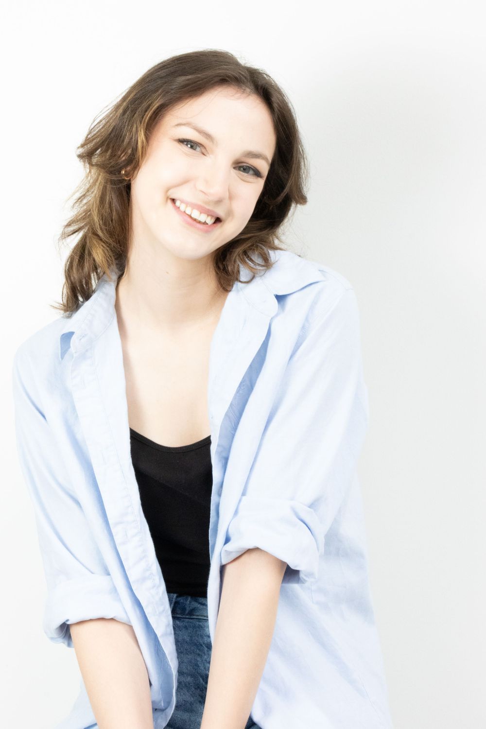 Smiling young woman in blue shirt and black top posing against white background.