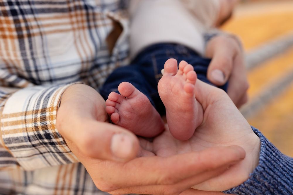 Tiny baby feet resting in gentle adult hands wearing plaid.