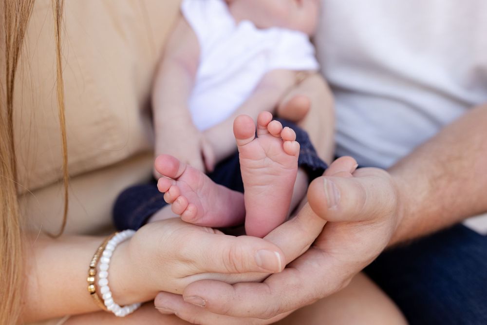 Tiny baby feet being held gently in adult hands against neutral background.