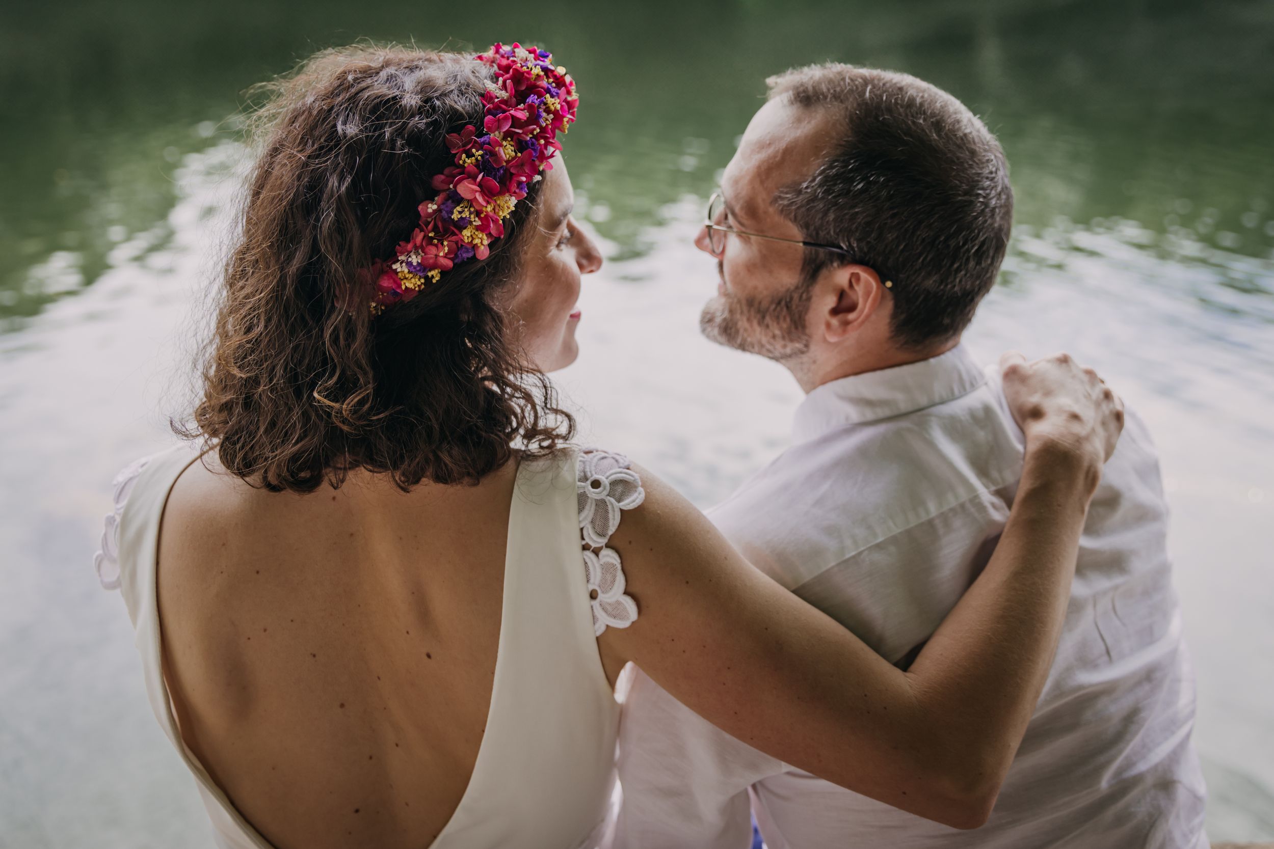 Des mariés assis au bord de l'eau se regardent amoureusement, bras dessus bras dessous
