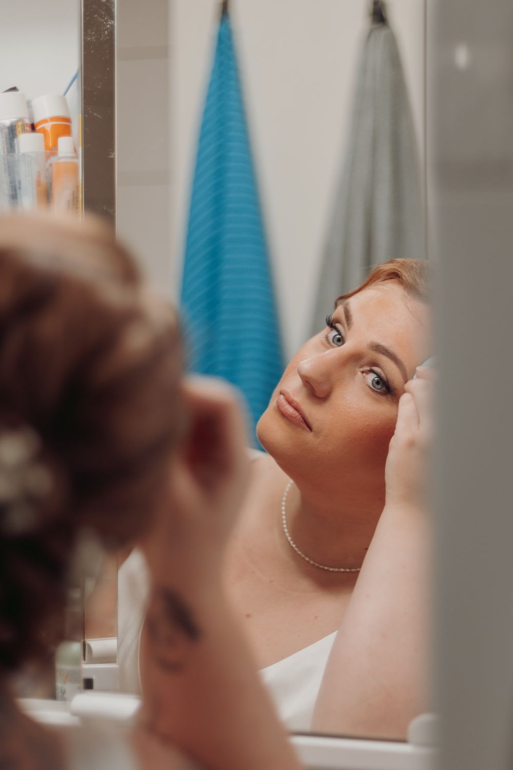 Close-up reflection of someone preparing hair and makeup in a bathroom mirror.
