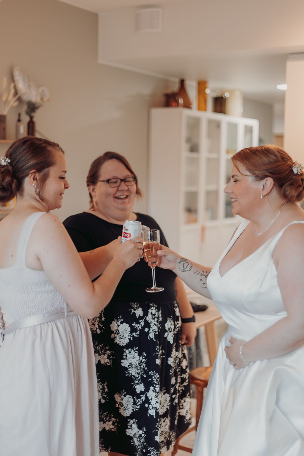 Group getting ready in white dresses and floral attire indoors.