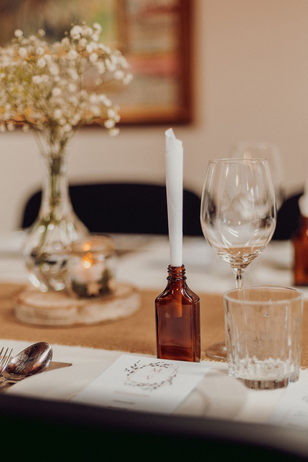 Elegant table setting with wine glasses, baby's breath flowers, and amber bottles.