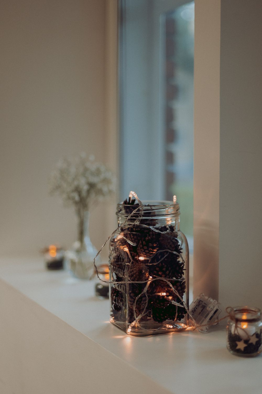 Moody candlelit windowsill with fairy lights in glass jars creating ambient lighting.
