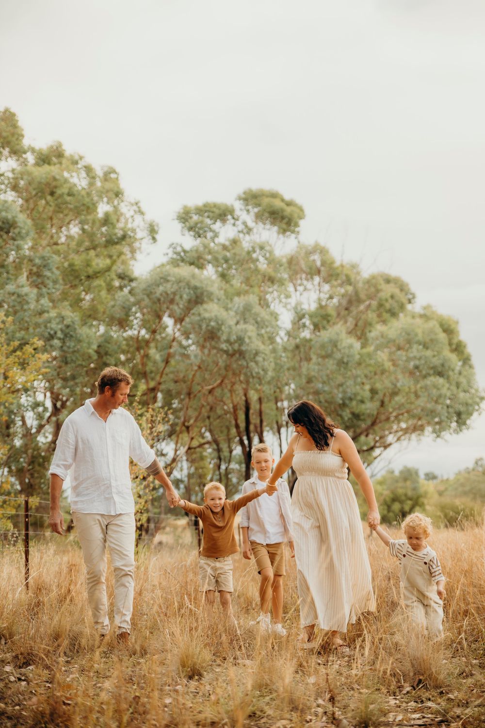 Family of five walking through golden grass field with eucalyptus trees, pregnant mother in white dress.