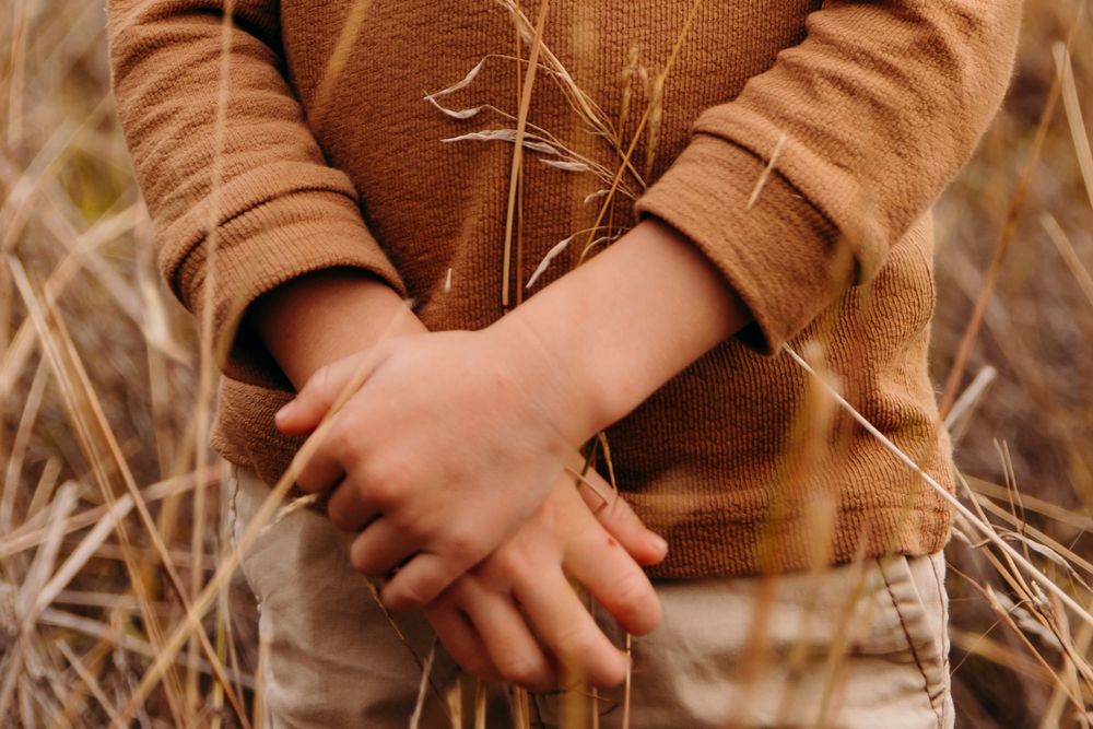 Close-up of young child with clasped hands standing in dry golden grass field.