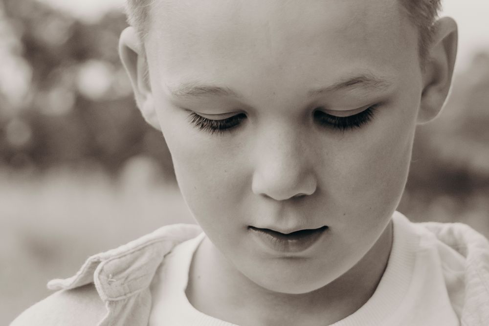 Close-up black and white portrait of a young child with long eyelashes looking downward.