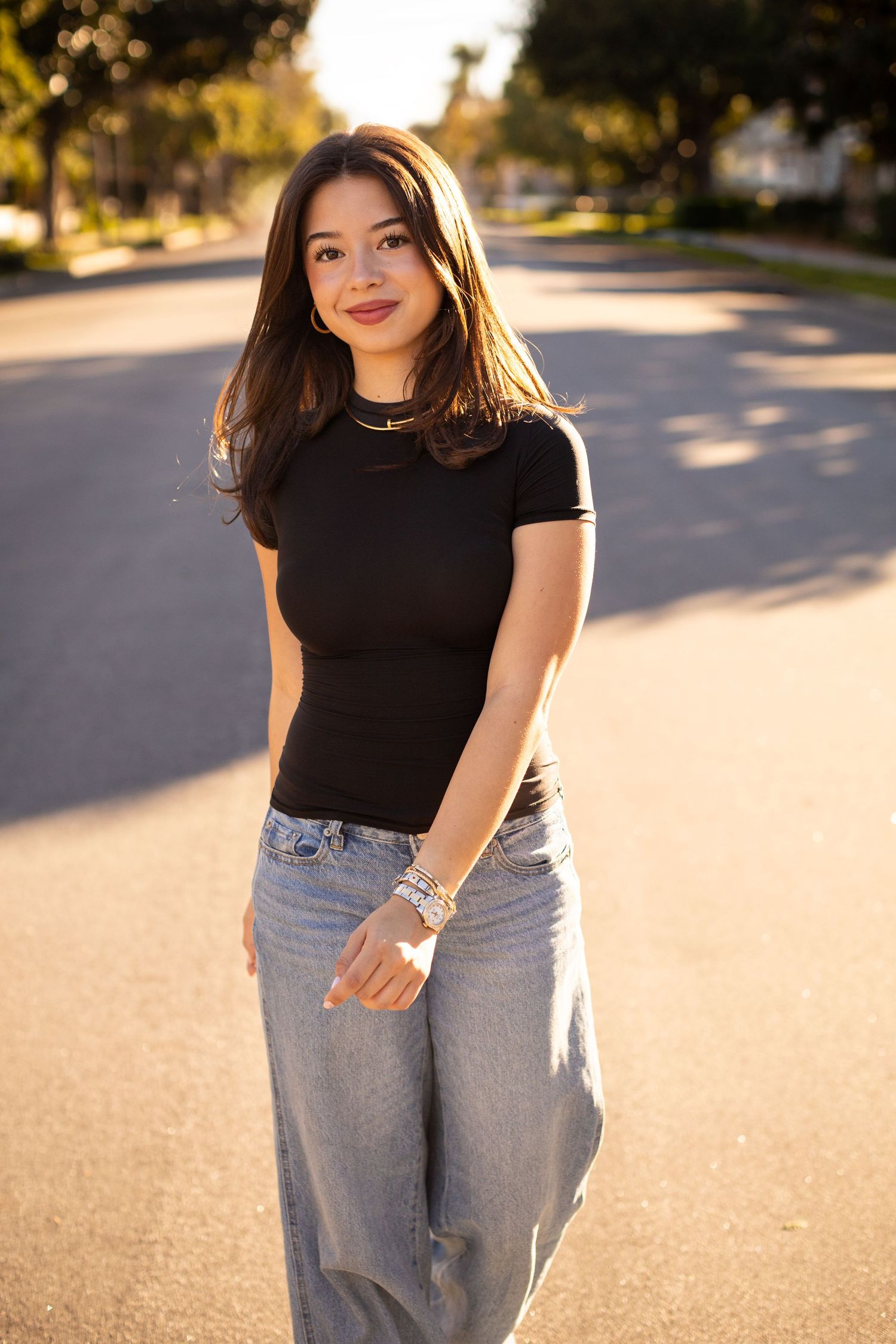 A high school senior in denim skirt and jean jacket posing under white columned architecture.