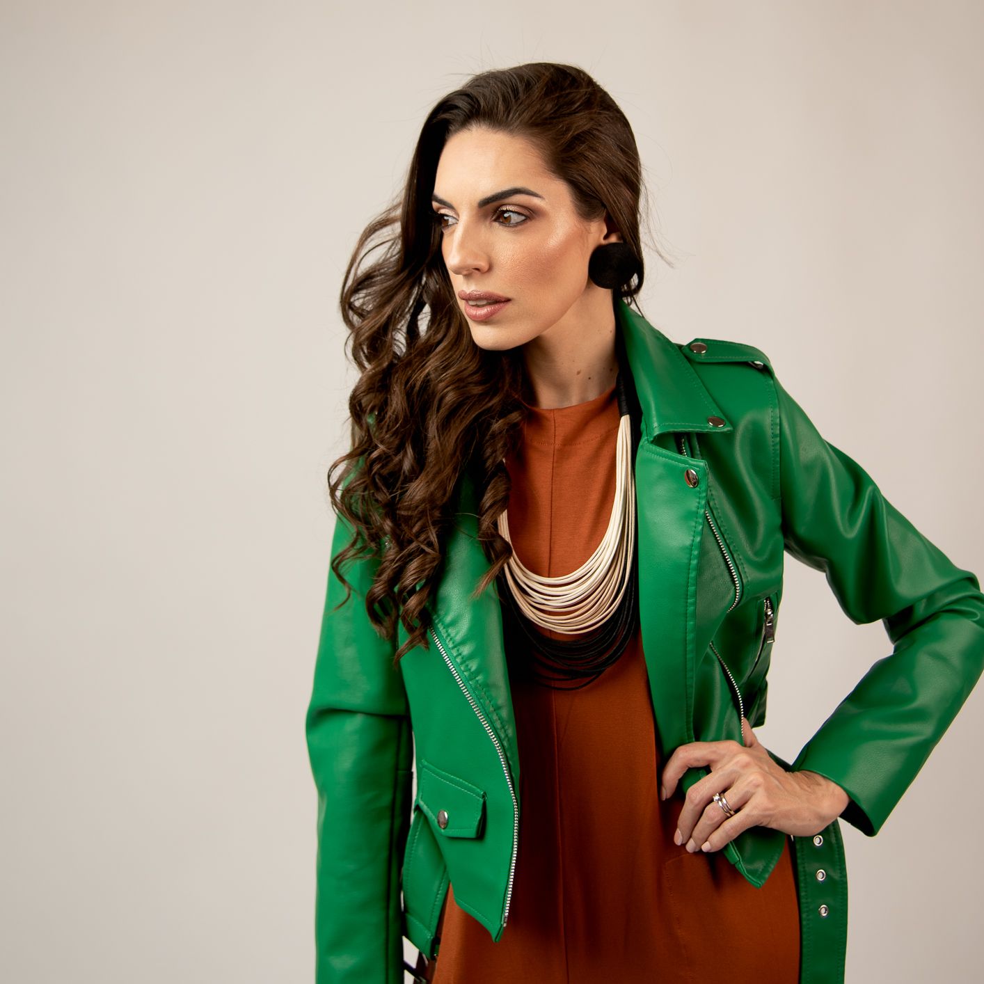 Stylish fashion portrait featuring emerald green jacket and rust-colored dress with layered necklaces.