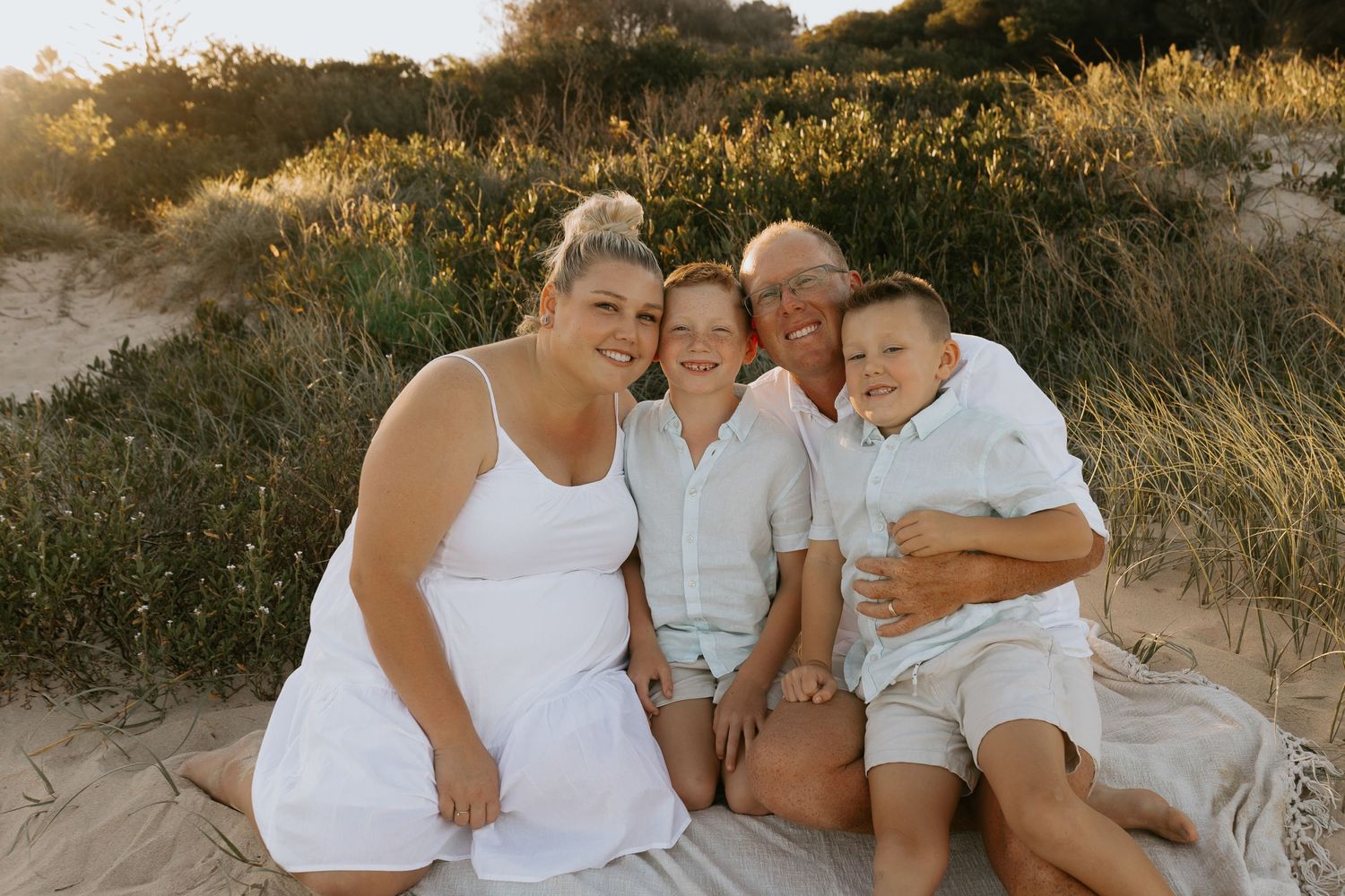 Family wearing white outfits poses together in a sunlit field.