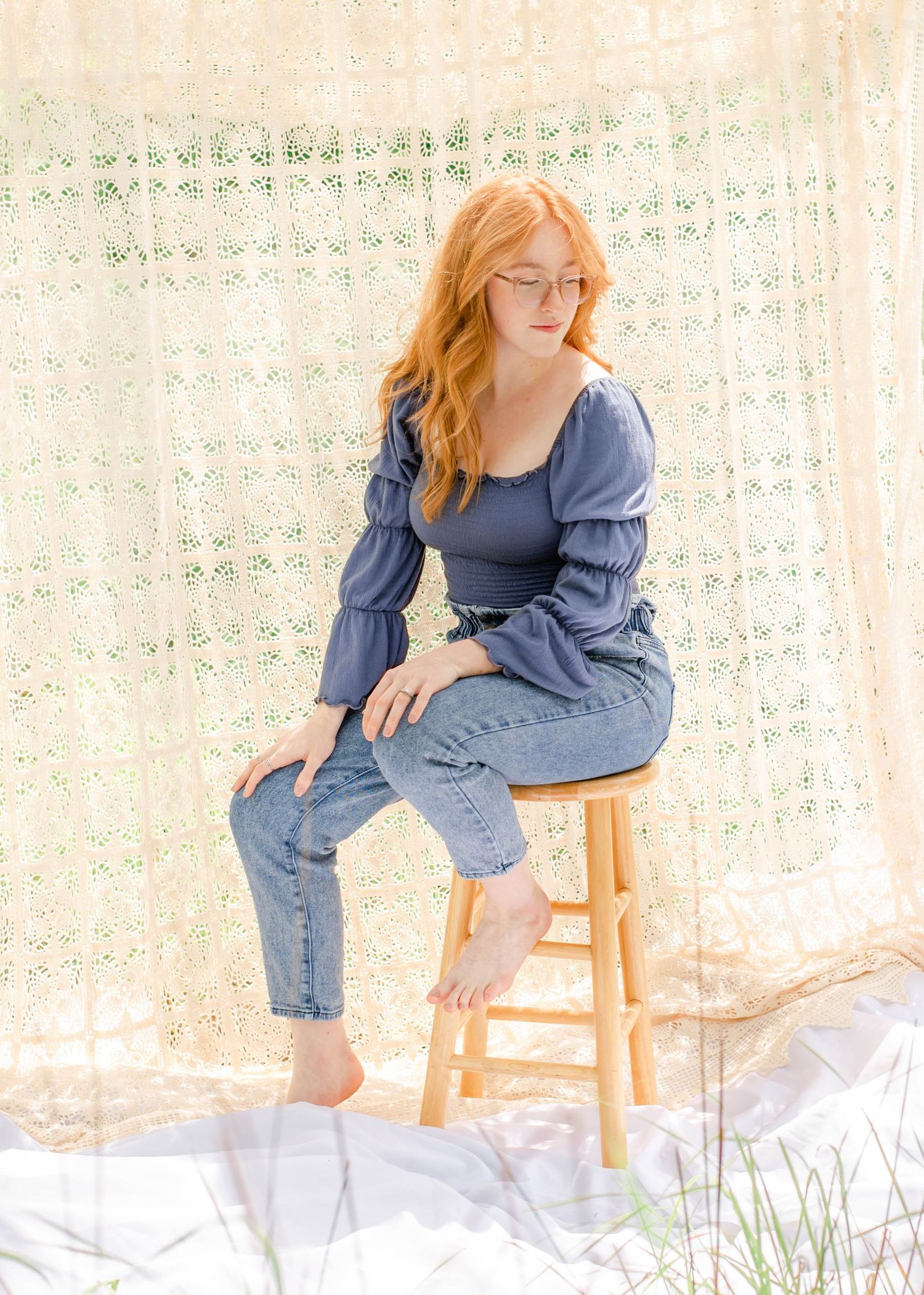 Natural light portrait with subject seated on wooden stool against delicate lace curtain.