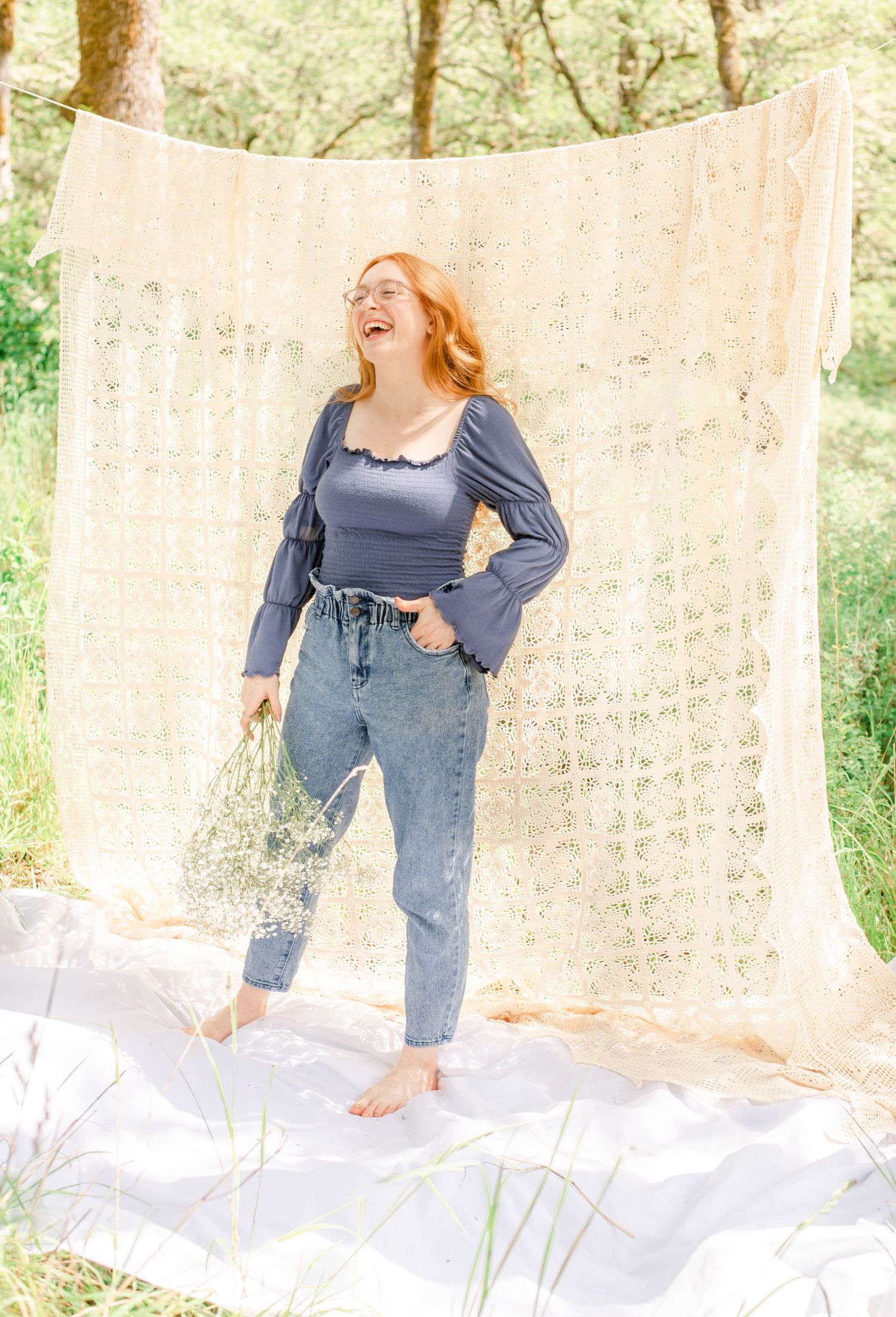 Joyful outdoor portrait in blue top and denim against cream lace curtain.