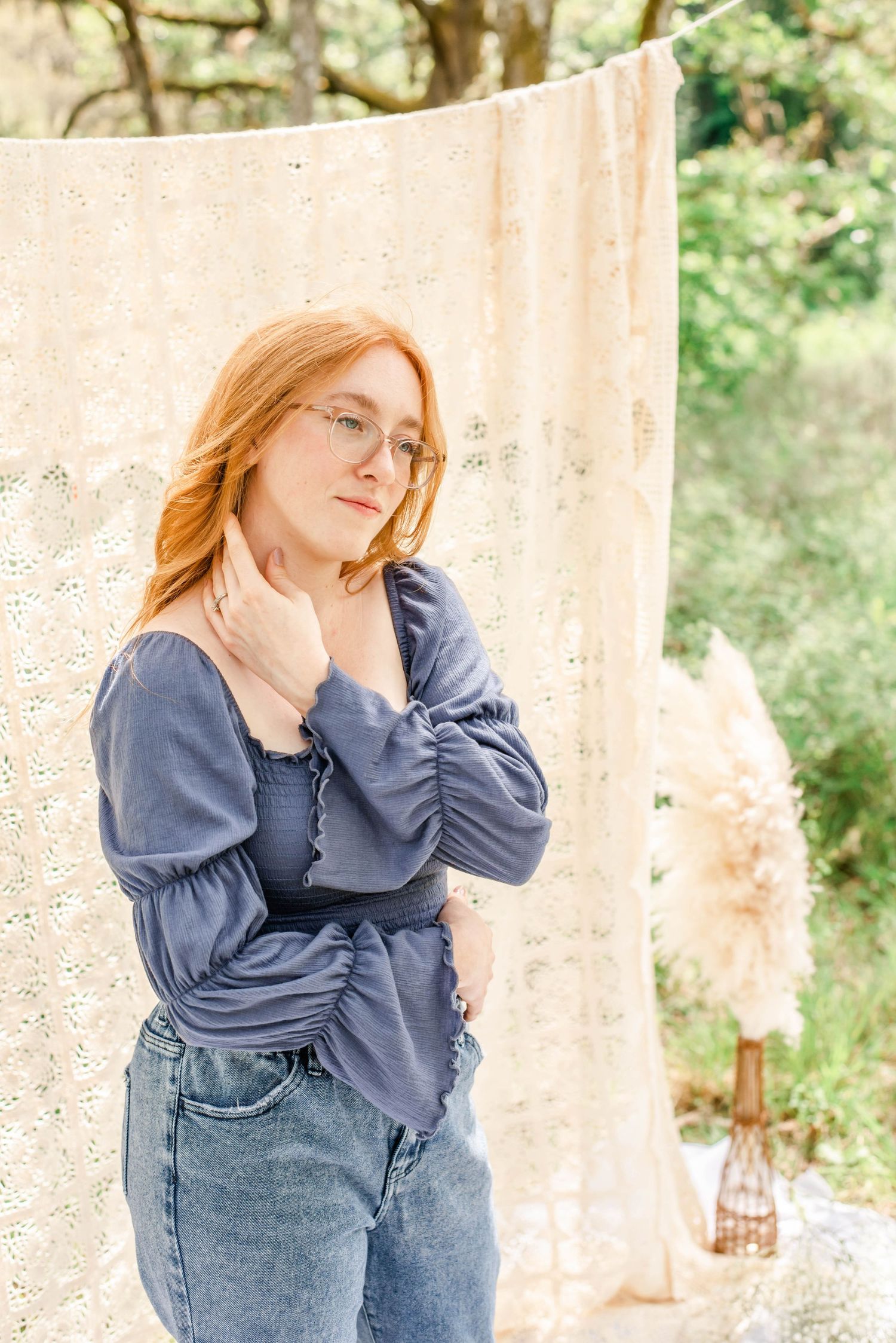 Person in denim lounges on white blanket during outdoor photoshoot.
