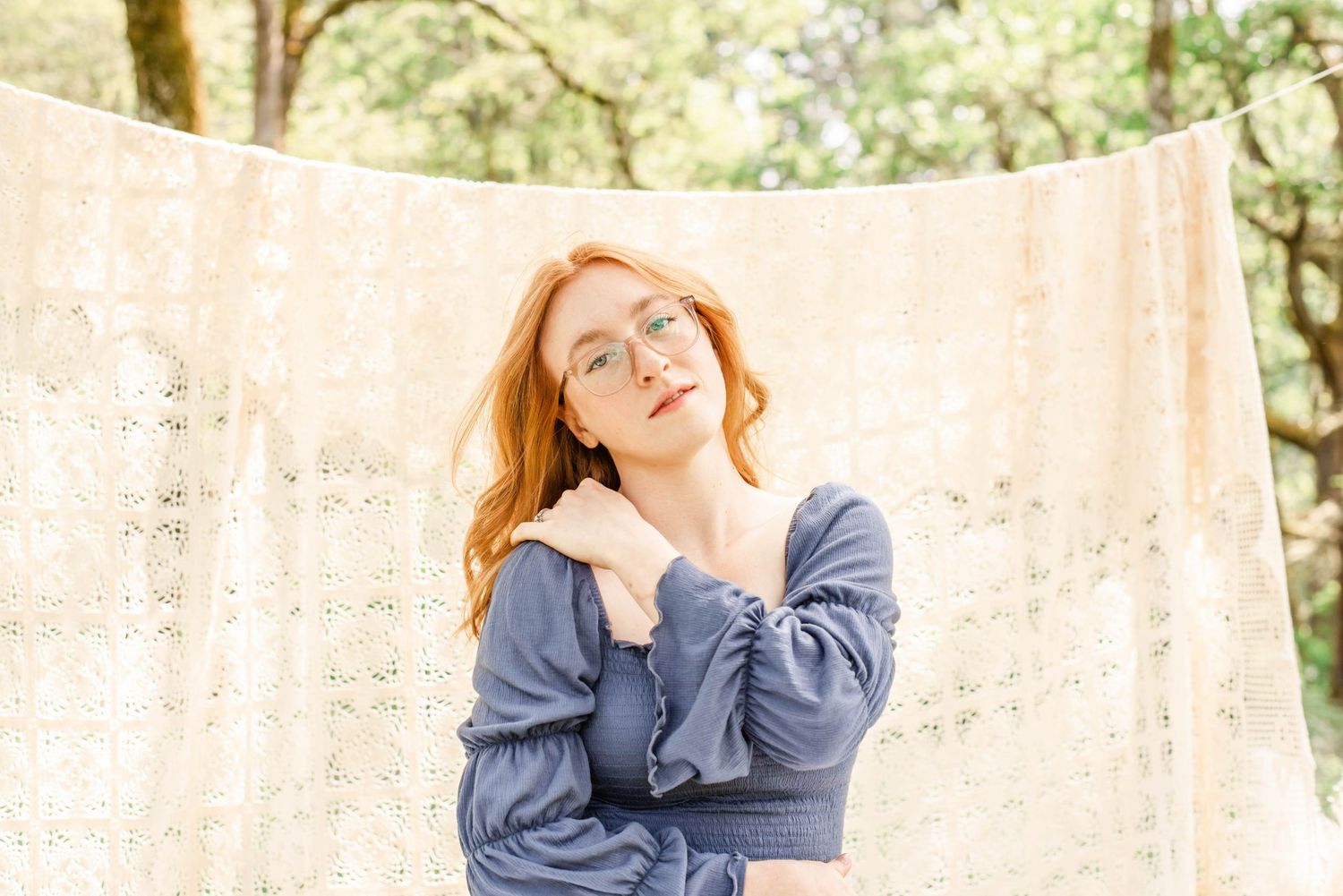 Person in blue denim outfit sits casually against cream backdrop in outdoor portrait session.