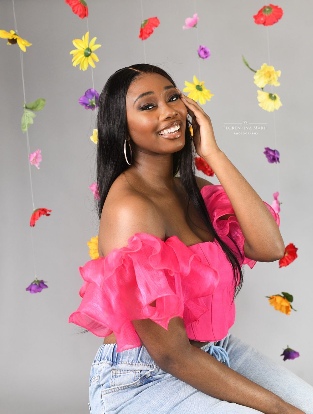 Studio portrait with vibrant flowers featuring a pink ruffle top and denim against a grey backdrop.