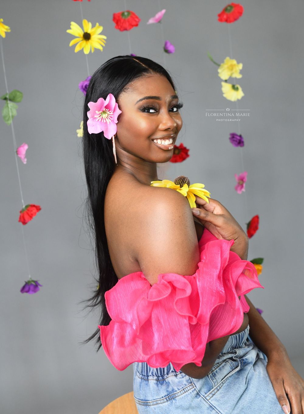 Colorful portrait with floating flowers featuring pink off-shoulder top and casual denim style.