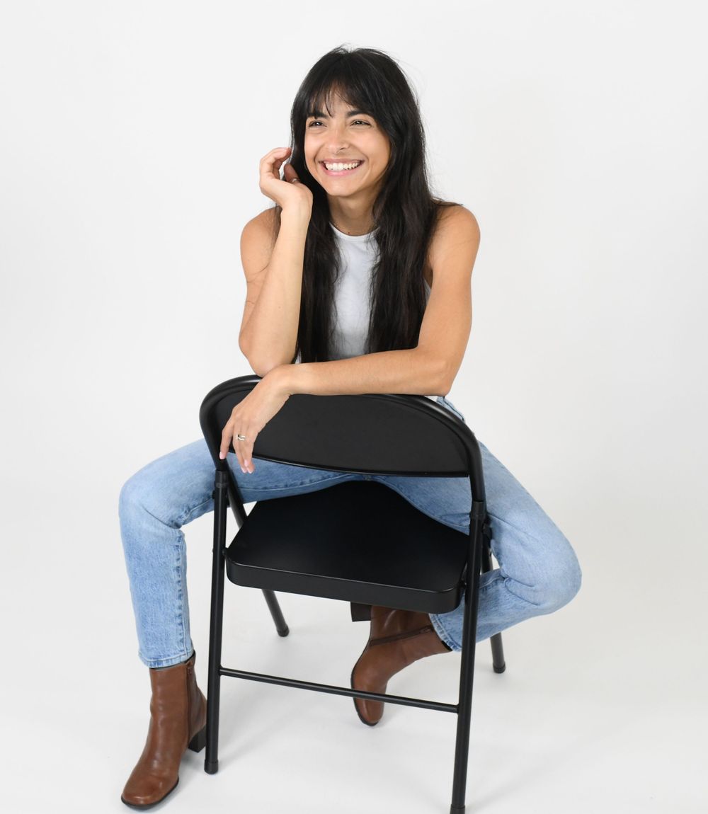Studio portrait on a black folding chair wearing jeans and a white top.