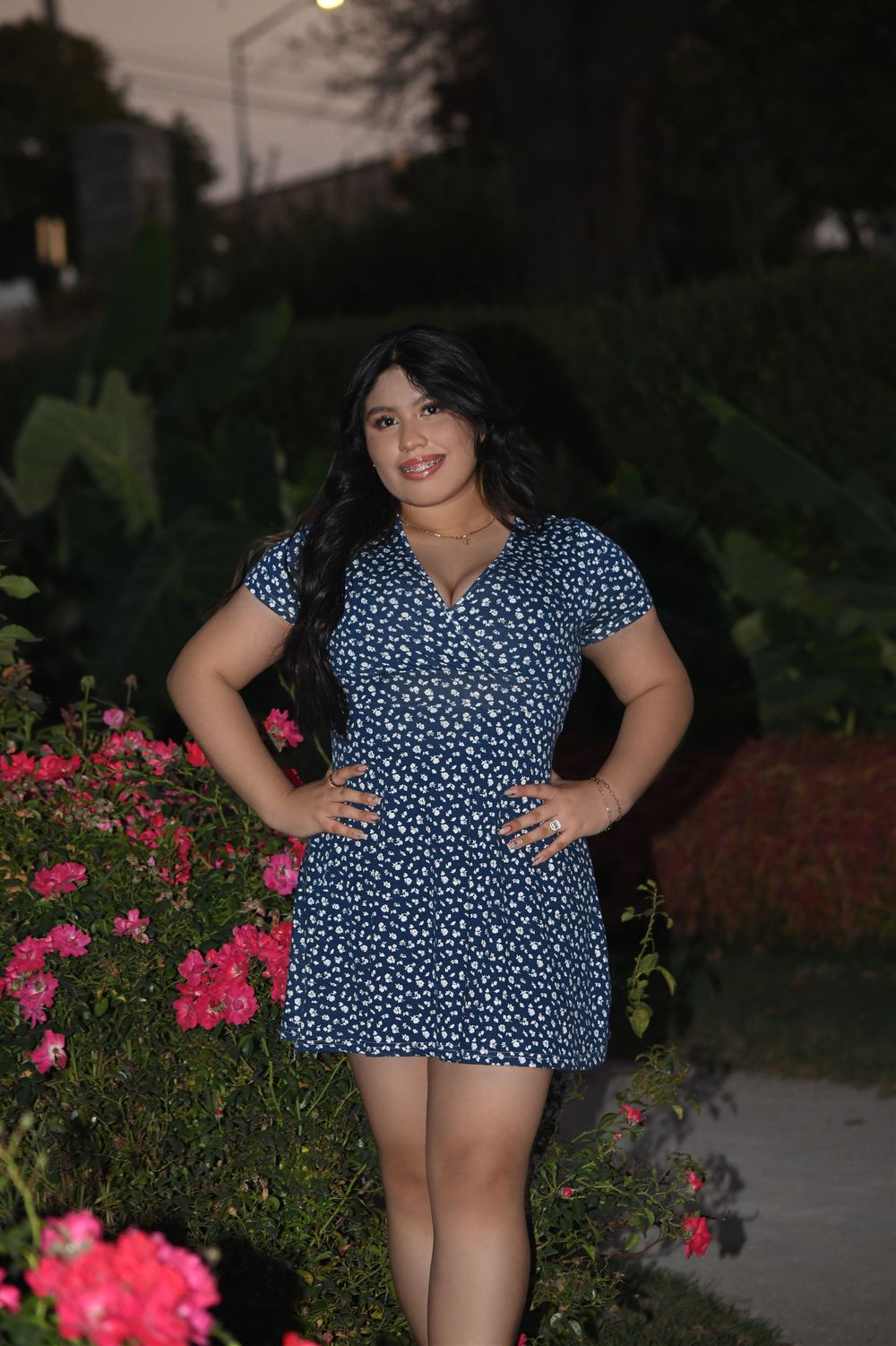 Portrait by pink flowers wearing a blue polka dot dress at dusk.