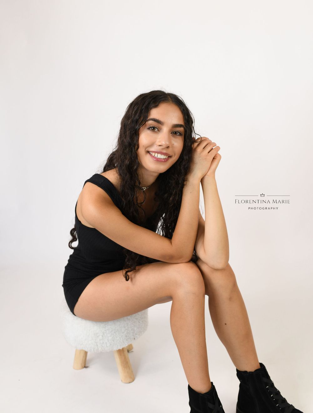 Casual portrait on wooden stool wearing black outfit and boots.