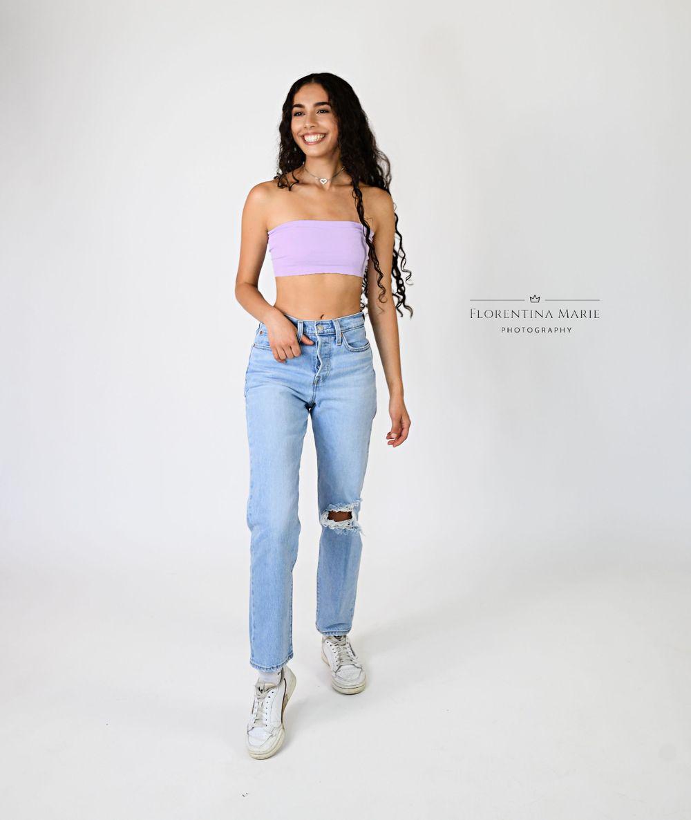 Fashion portrait in light wash denim and pink crop top against white background.