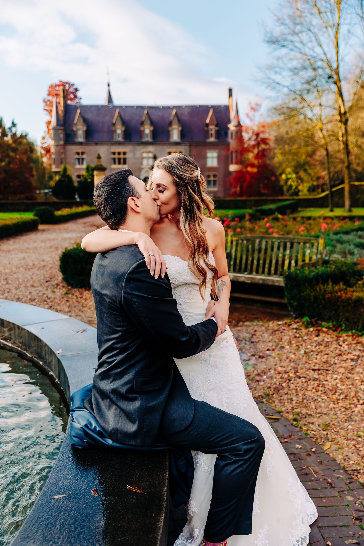 Intimate wedding moment shared between couple sitting on fountain edge with castle in background.