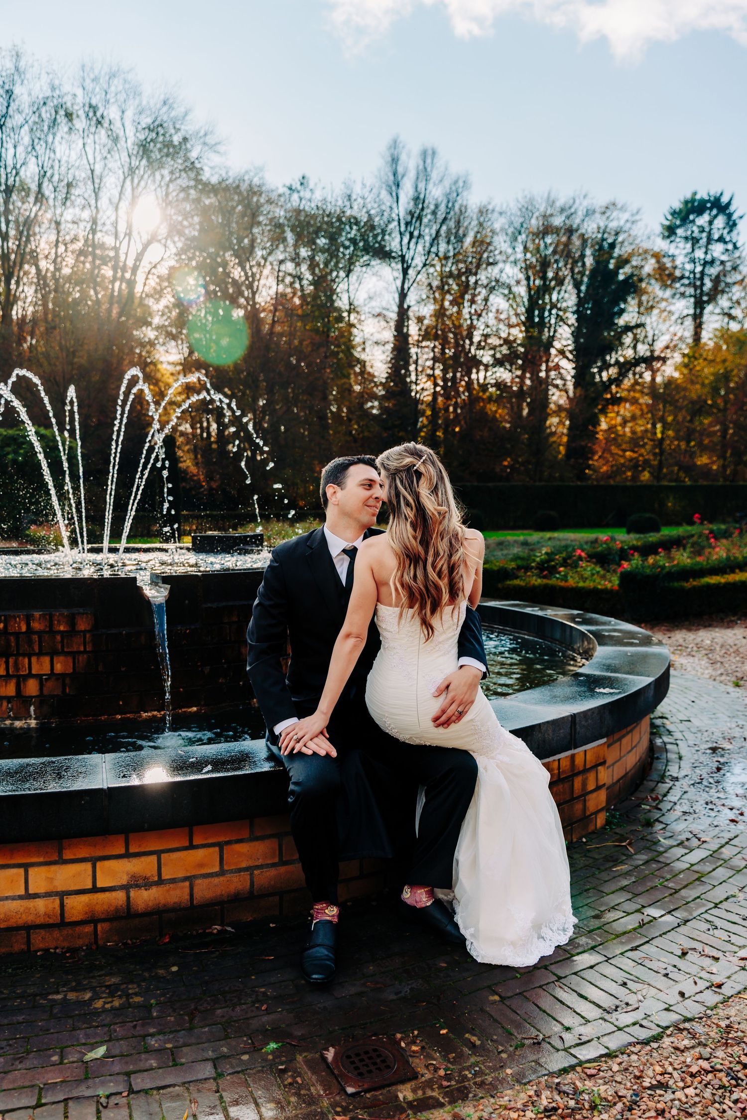 A romantic scene by a fountain with a couple sitting together at sunset in formal attire.