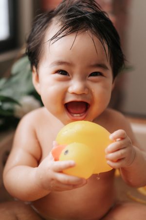 Excited baby holding yellow rubber duck while taking a bath.興奮的寶寶抱著黃色橡皮鴨洗澡。