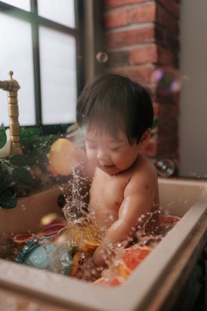 Baby splashing and playing in sink with colorful toys寶寶在水槽裡玩水，手裡拿著色彩鮮豔的玩具。