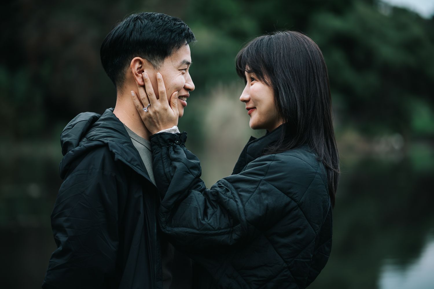 A young couple share a tender moment outdoors, with the woman gently touching the mans face after a surprise proposal in Melbourne.