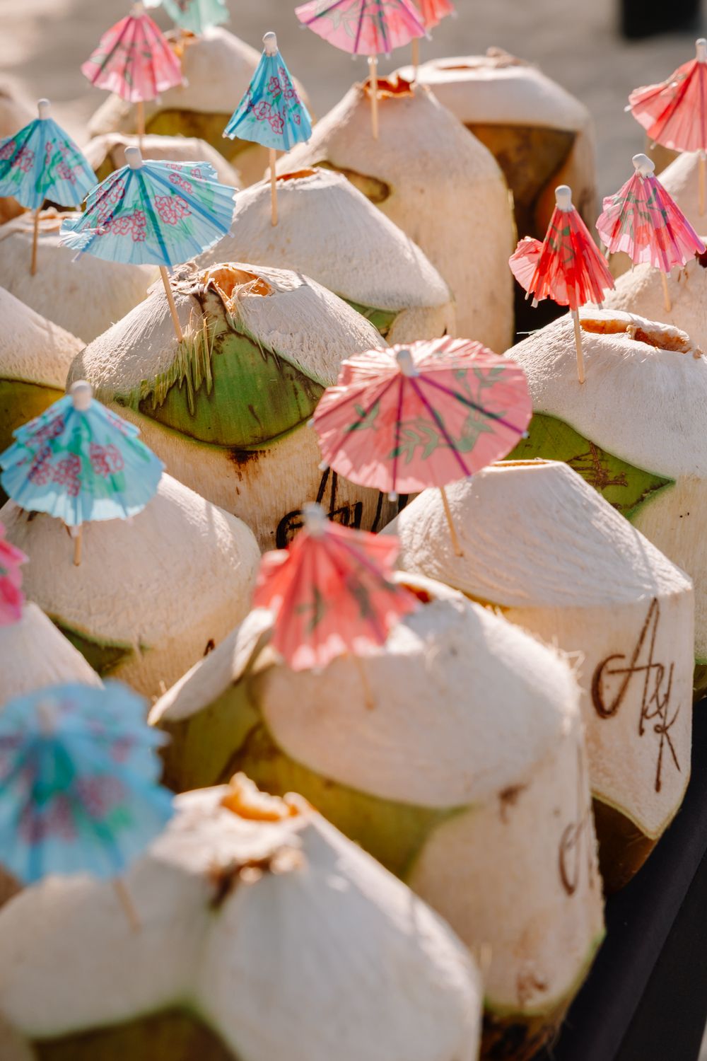 Fresh young coconuts topped with colorful cocktail umbrellas served as tropical drinks at an outdoor market.
