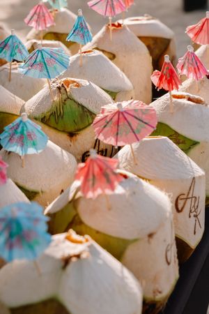 Fresh young coconuts topped with colorful cocktail umbrellas served as tropical drinks at an outdoor market.