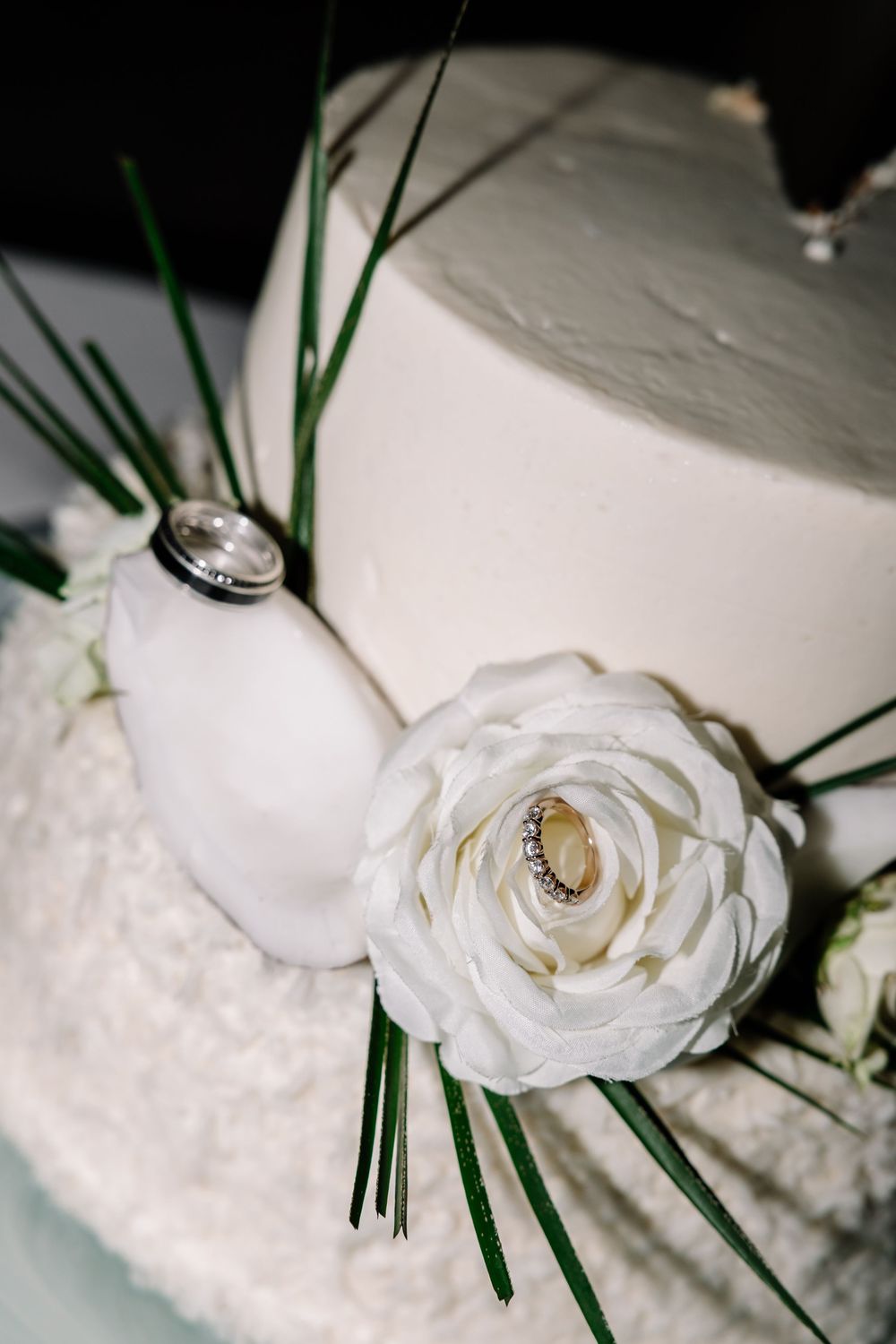 Elegant two-tier white wedding cake with roses and rings on top.