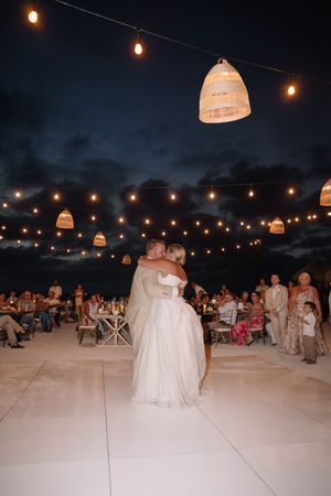 Bride and groom share first dance under string lights and wicker lanterns at an outdoor evening wedding reception.