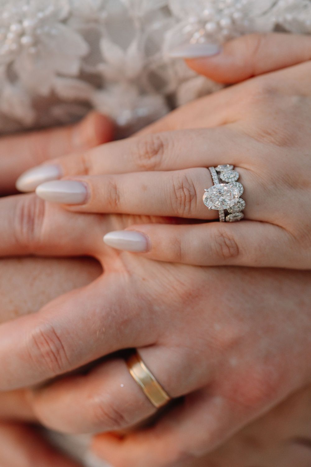 Close-up of bride and groom hands showing diamond engagement ring, wedding band stack, and gold wedding band.