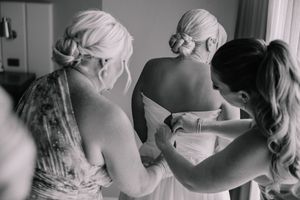Bridesmaids helping bride button up wedding dress in black and white photo.