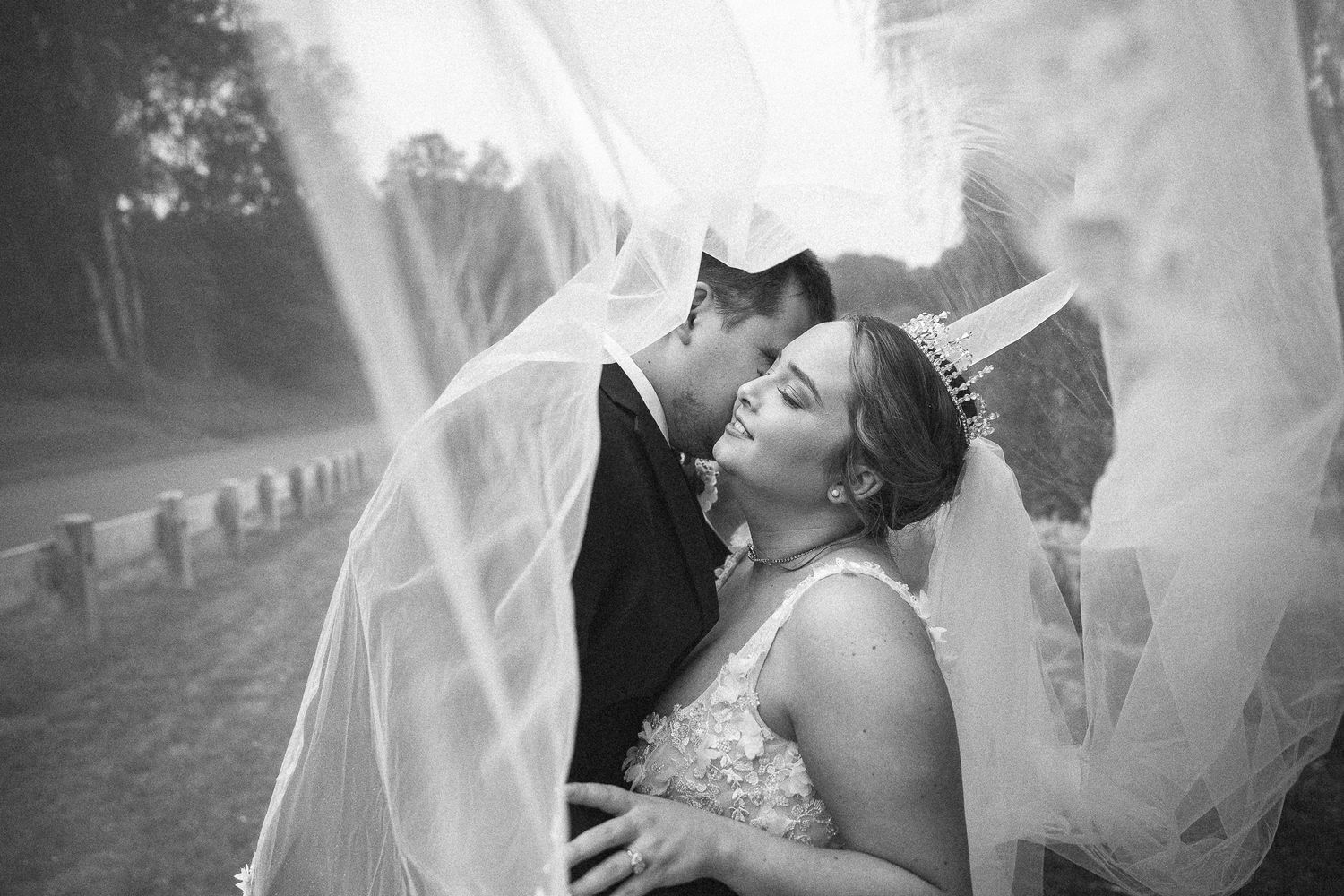 A bride and groom share a romantic kiss in a forest wedding setting with bokeh fairy lights in the foreground.