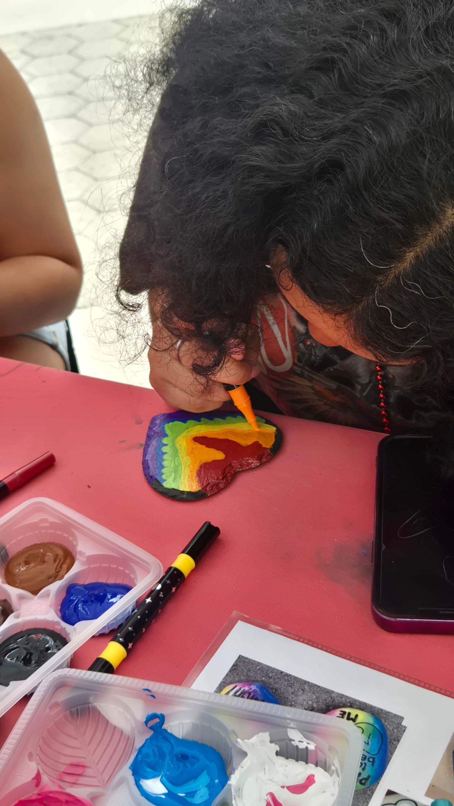 Person painting a colorful rainbow design on a pink surface with art supplies nearby.