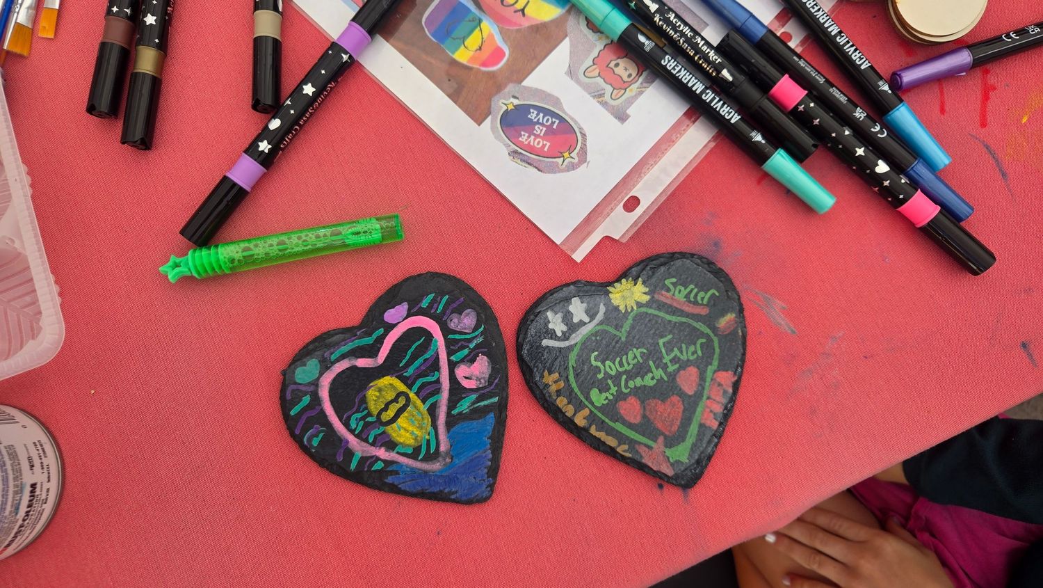 Heart-shaped chalkboard art pieces with colorful marker designs on a pink table surrounded by Tombow dual brush pens.