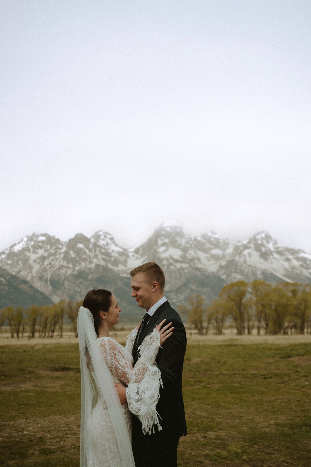 Bride and groom share a romantic moment in front of snow-capped Grand Teton mountains on their wedding day.