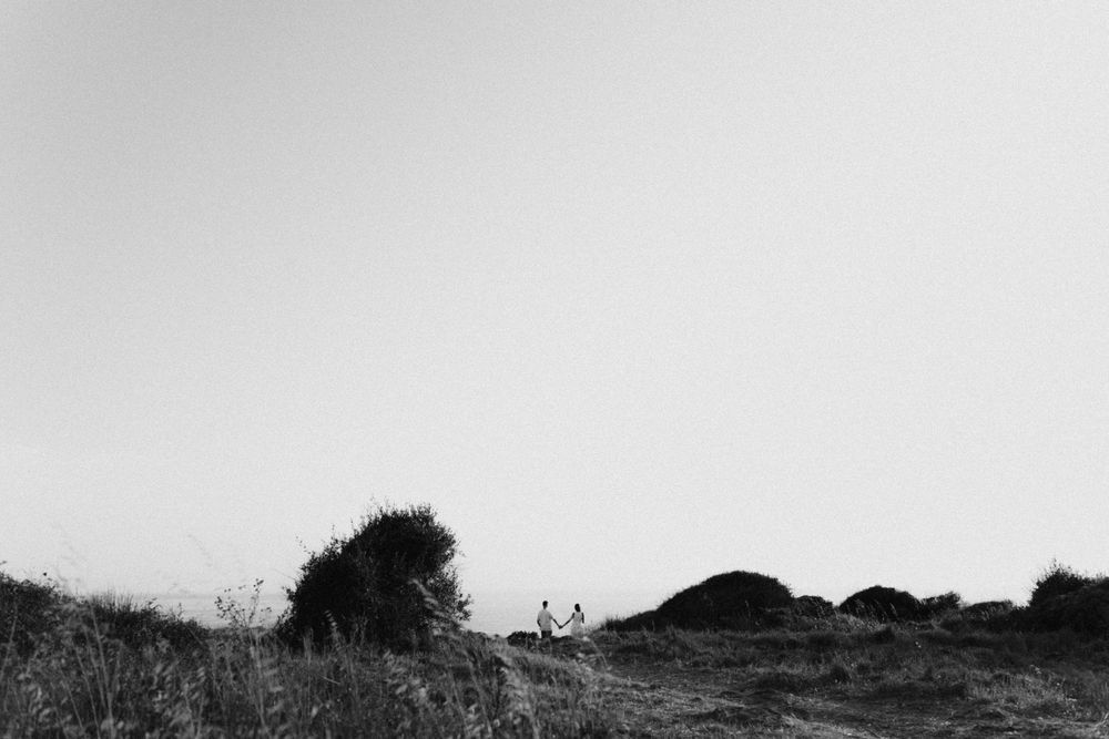 Couple walks through scenic rural landscape with haystacks in minimalist black and white photography.