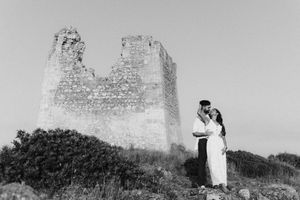 Couple embraces romantically before ancient stone tower ruins in black and white outdoor portrait.