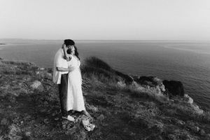 Woman in white dress standing alone on a seaside cliff in black and white.