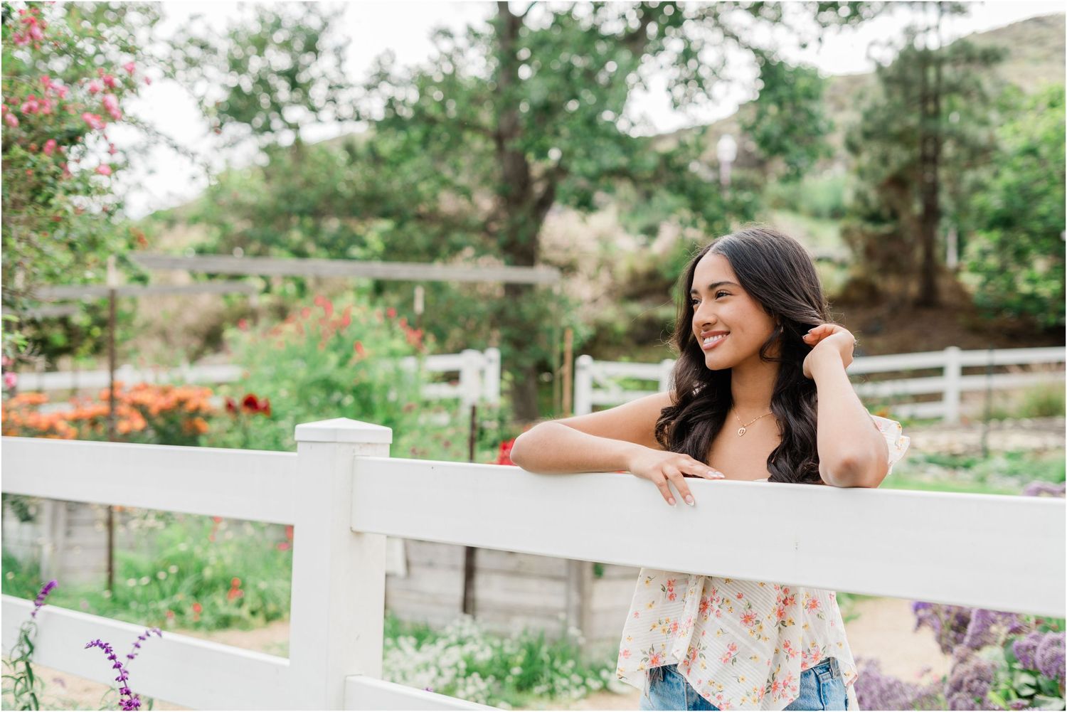 Senior photos at Madonna Inn Gardens with a SLO senior photographer featuring a floral tank, jeans, and lush garden scenery.
