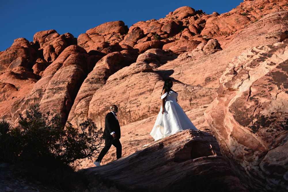 Bride and groom walking on red rock canyon formations during a desert elopement photoshoot in Nevada.