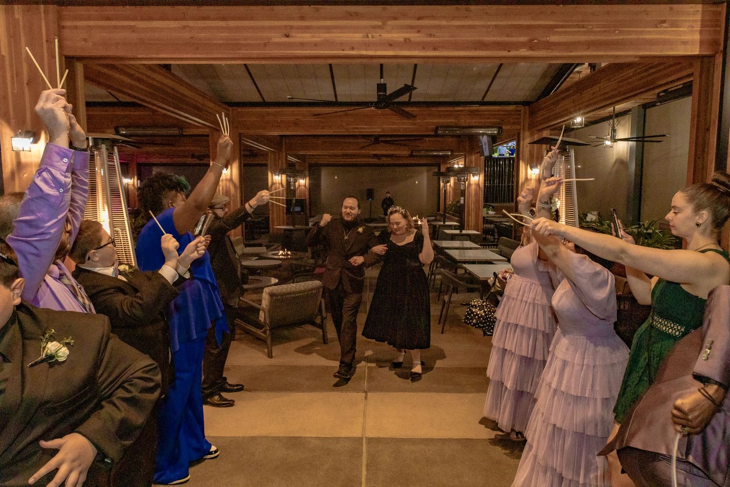 Wedding couple walks through sparkler tunnel with guests in formal attire at elegant indoor reception venue.