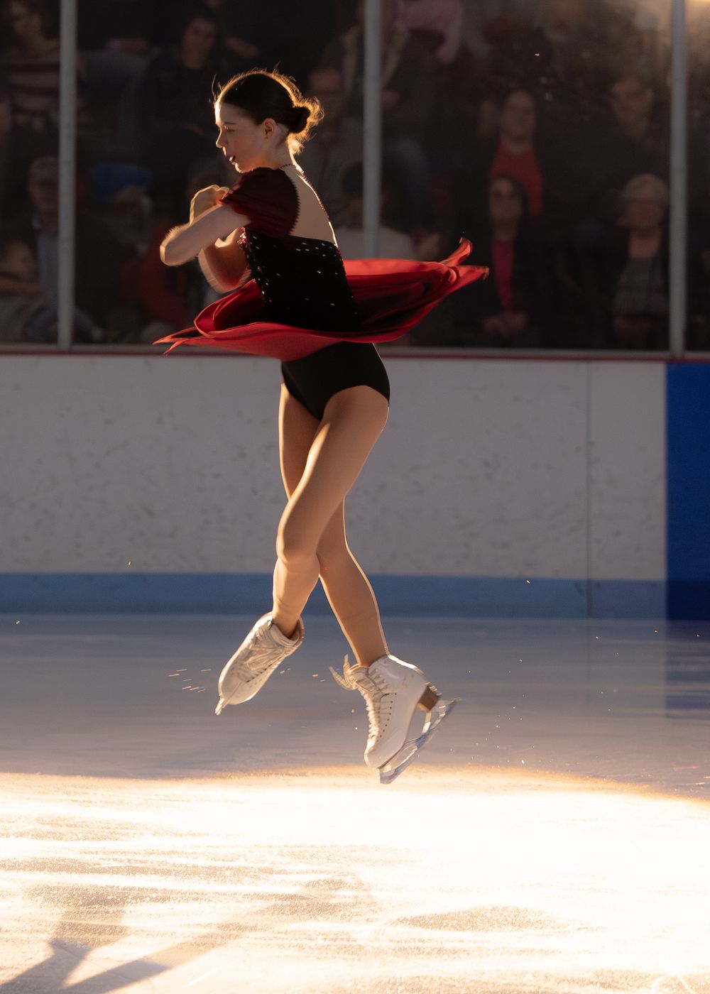 Female figure skater in black and red dress captured mid-jump during outdoor ice skating performance. Hagerstown, Maryland.