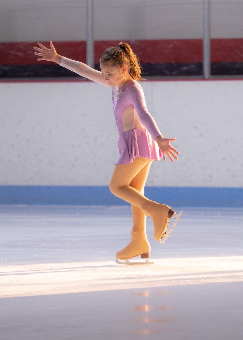 Young girl figure skater in pink and purple costume balancing gracefully on outdoor ice rink. Hagerstown, Maryland.