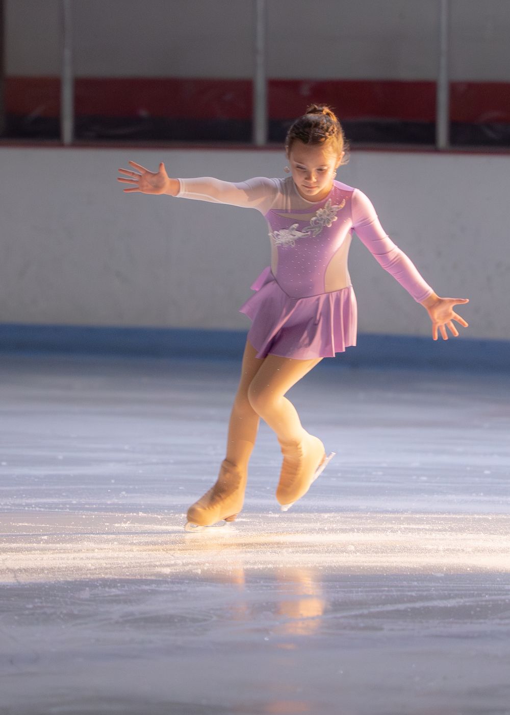 Young girl figure skater in purple dress performing with arms outstretched on an indoor ice rink. Hagerstown, Maryland.