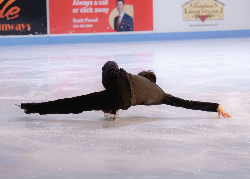 Figure skater performing a dramatic split position on ice during a competition. Hagerstown, Maryland.